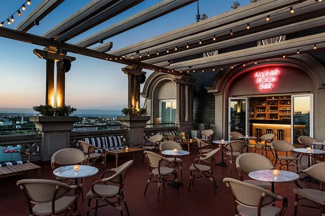 The Alvear Roof Bar at dusk, its terrace tables under a pergola of lights with the neon sign over the bar