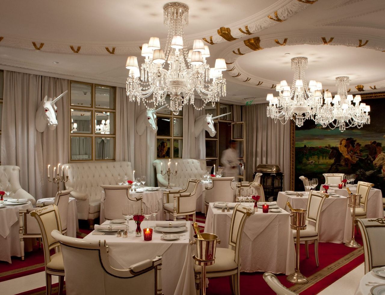 The white-and-red dining room of Bistro Sur at the Faena Hotel, with chandeliers and unicorn heads on the walls