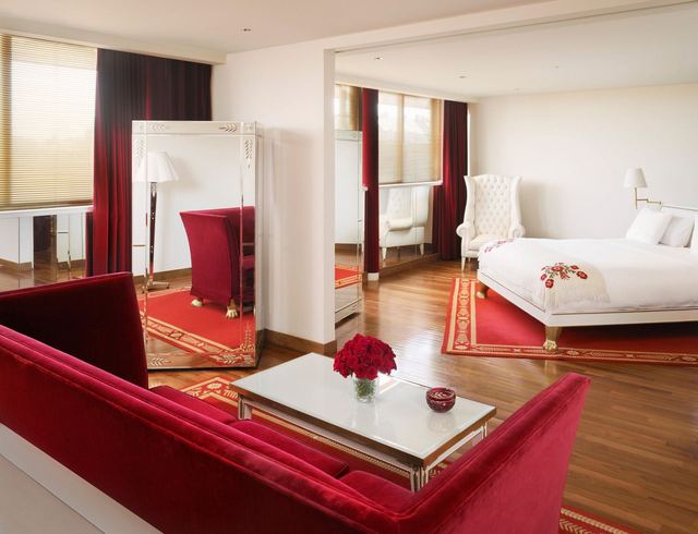 A suite at the Faena Hotel, with a red velvet sofa, red rugs and a white bed